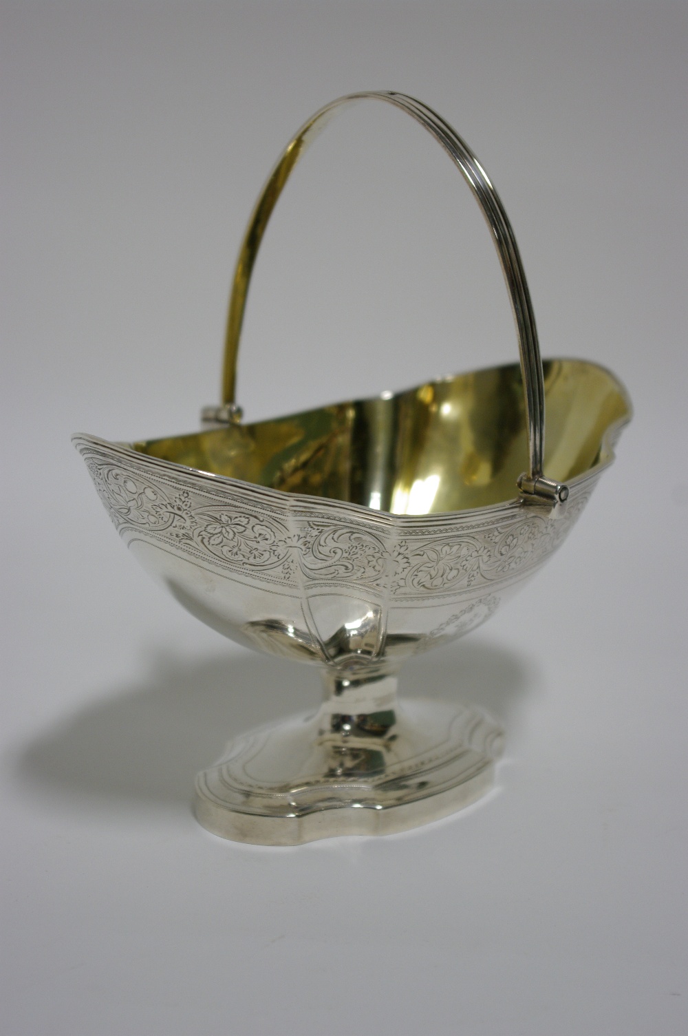 A George III oval fluted sugar basin with swing handle, parcel-gilt interior, engraved floral