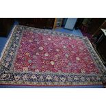 A Persian carpet of madder ground, with all-over multi-coloured meandering floral design within wide