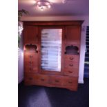 An unusual Edwardian oak combination wardrobe enclosed by a centre mirror-panel door, the angled