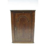 A late 18th century oak hanging corner cabinet enclosed by a fielded round-arch panel door; 28¾"