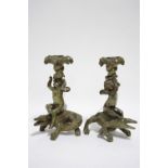 A pair of cast brass candlesticks in the form of cherubs holding cornucopia, riding on the backs