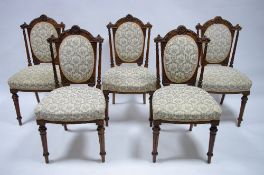 A set of five Victorian carved walnut frame dining chairs with padded oval backs, wide padded