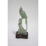 A Chinese carved pale green jade model of an exotic long-tailed bird perched on a tree-stump, 6½”