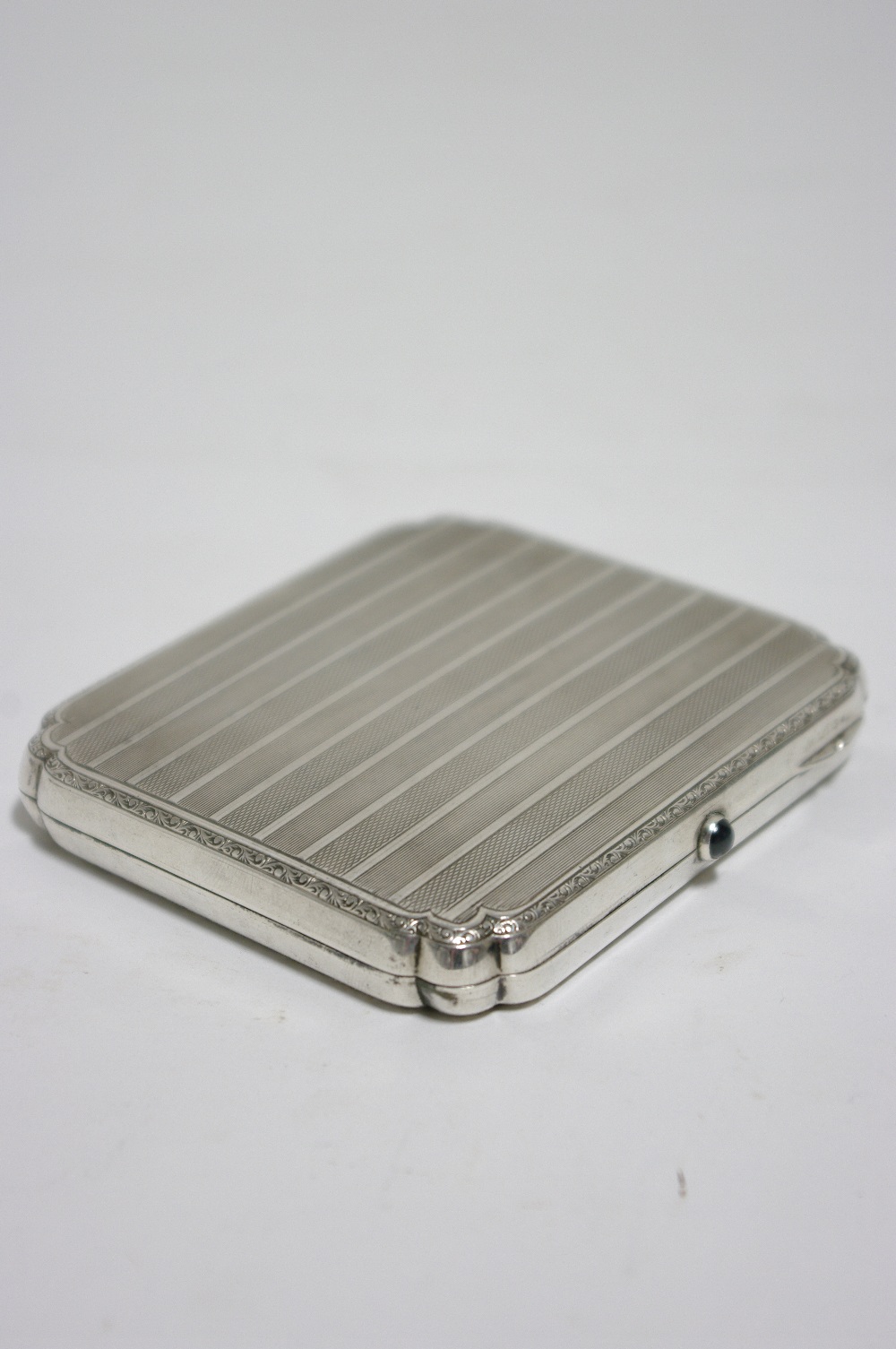 A rectangular engine-turned pocket cigarette case with re-entrant corners & blue hardstone push-