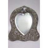 An Edwardian heart-shaped table mirror with easel support, the wide border pierced & embossed with