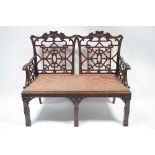 A pair of “Chinese Chippendale” two-seater settees with fretwork splats to the open backs, padded