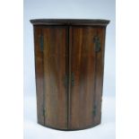 A late 18th century oak & mahogany crossbanded bow-front hanging corner cupboard enclosed by pair of