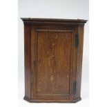 A late 18th century oak hanging corner cupboard enclosed by a panel door, & with canted corners;