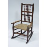 A 19th century ash rocking elbow chair with turned spindle rail back, rush seat, & on turned legs.