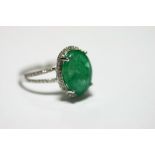 AN EMERALD & DIAMOND RING, the oval emerald measuring 13mm x 10mm, the border & split shoulders