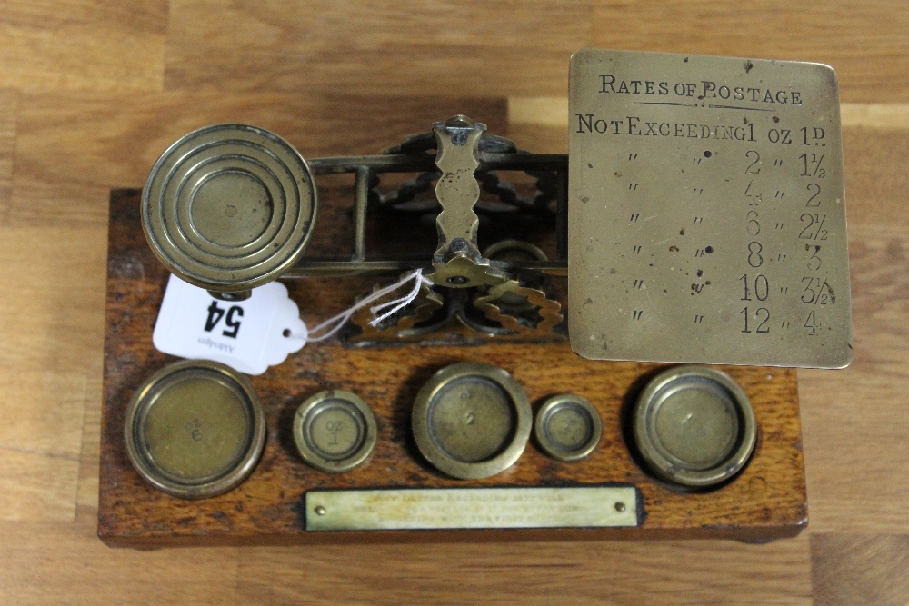 An early 20th century brass postal scale mounted on oak plinth base with bun feet, and with five