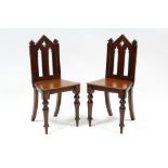 A pair of Victorian mahogany hall chairs with gothic pierced backs, hard seats & on turned tapered