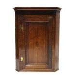 A late 18th century oak hanging corner cupboard with canted corners, enclosed by a panel door with