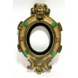 A carved giltwood oval picture frame with satyr masks above & below, the border inset coloured paste