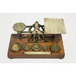 54. An early 20th century brass postal scale mounted on oak plinth base with bun feet, & with five