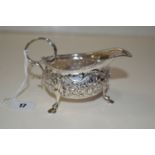 A silver sauce boat of helmet form, embossed with foliate decoration, standing on three hoof feet,