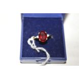 A synthetic ruby ring, the oval facet cut synthetic ruby flanked by white stones either side,