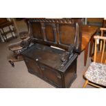 A dark stained oak monk's bench, the rectangular top hinged on lion pattern supports,