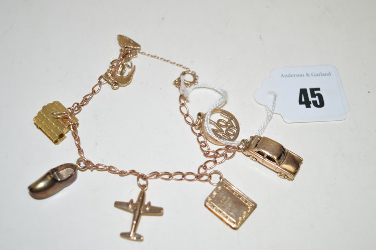 A yellow metal charm bracelet set with various charms, to include: palm tree, log cabin, clog,