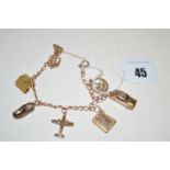 A yellow metal charm bracelet set with various charms, to include: palm tree, log cabin, clog,
