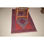 A Baluchi rug with geometric motif to red field and flower head design to border.