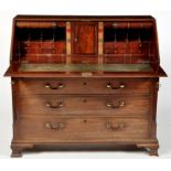 A George III mahogany bureau, the fall flap with inlaid stringing enclosing central cupboard door,
