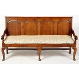 A late 18th Century oak settle, the arched panelled back above scrolling open arms,