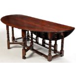 An 18th Century style oak wake table, the oval top with fall flaps, shaped frieze at each end,