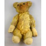 A small vintage plush teddy bear in very worn condition, with glass eyes and stitched nose,
