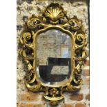 An early 19th century carved giltwood mirror with shaped bevelled plate, surmounted by an open shell