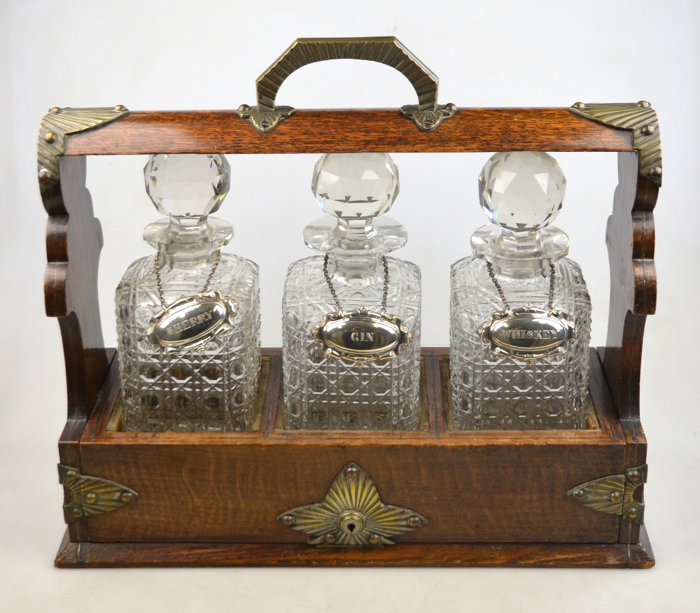 An Edwardian oak tantalus with plated mounts, fitted with three square-cut glass decanters (- locked