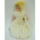 A wax-headed girl doll with blond wig and brown glass eyes, on stuffed body with wax fore-limbs,