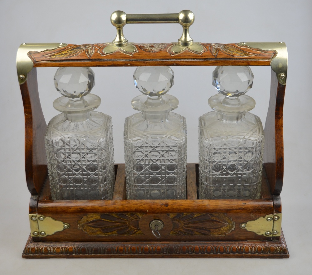 An Edwardian carved oak tantalus with plated mounts, containing three square cut glass decanters and