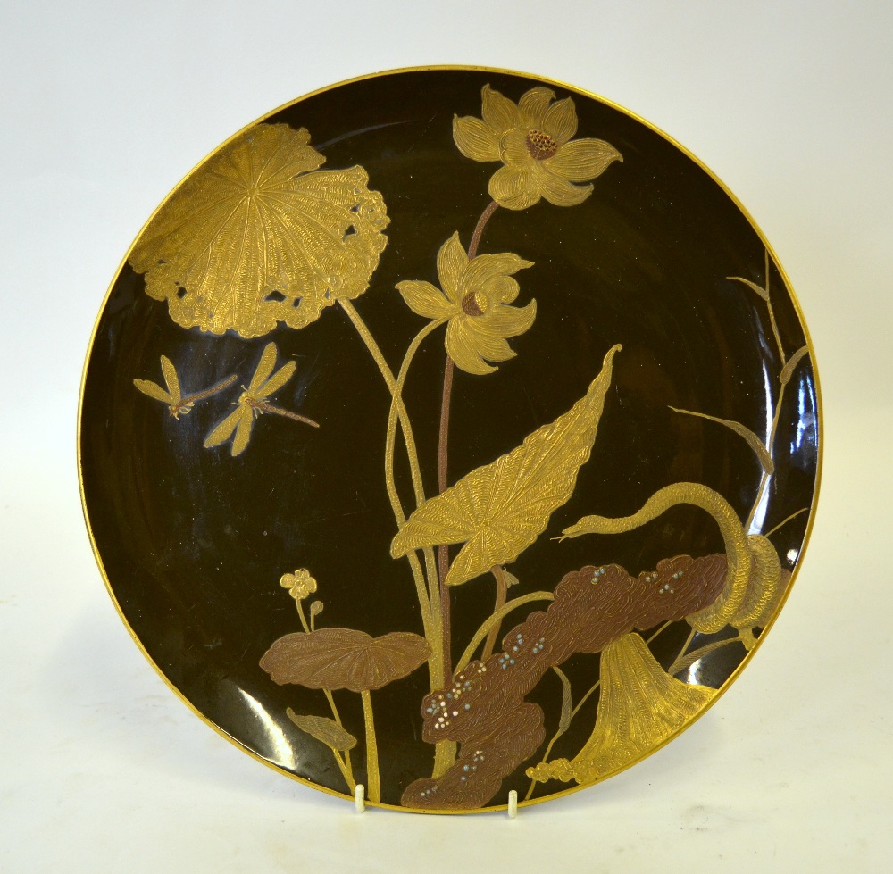A Japanese porcelain charger glazed to imitate lacquer, the brown ground painted in gilt with lotus,