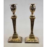 A pair of late Victorian Adam-style loaded silver candlesticks with urn tops on square baluster