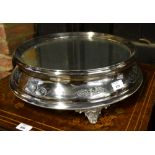 An epns circular wedding cake stand with mirror top, engraved sides and cast scroll feet,
