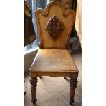 A Victorian oak hall chair having an arched back centred by a relief carved armorial device,