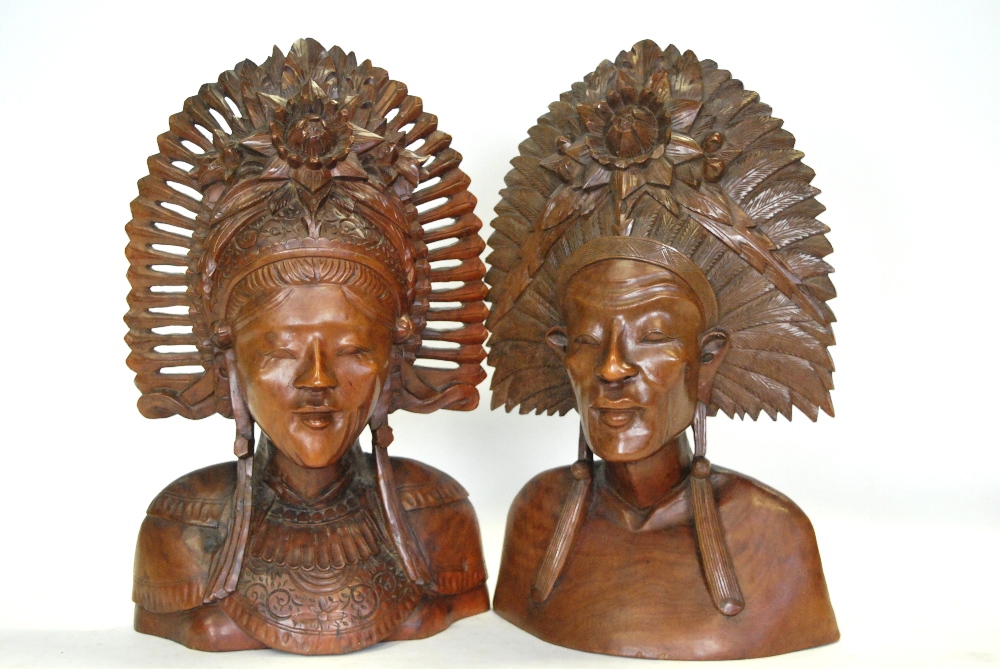 A pair of Balinese carved wood busts with ornate head-dresses,
