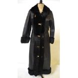 A long length black leather coat with black fur collar, cuffs, edges and hem, with gilt metal