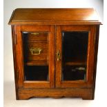 An Edwardian oak smokers cabinet with pair of bevelled panel glazed doors enclosing drawers,