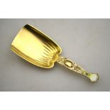 A US sterling silver gilt and enamel caddy spoon with shovel bowl and foliate scroll handle,