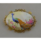 An oval ceramic brooch, painted with a peacock on a stone parapet, signed C. Gresley, including gilt