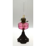 An oil lamp with cut cranberry glass font and foliate cast base