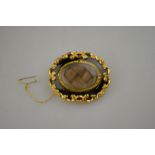 An oval mourning brooch having central hairwork with black enamel surround in gold scrollwork