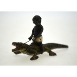 A cold-painted metal miniature figure of a boy riding a crocodile,