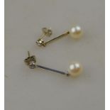 A pair of whte metal and cultured pearl drop earrings hanging from a single diamond stud