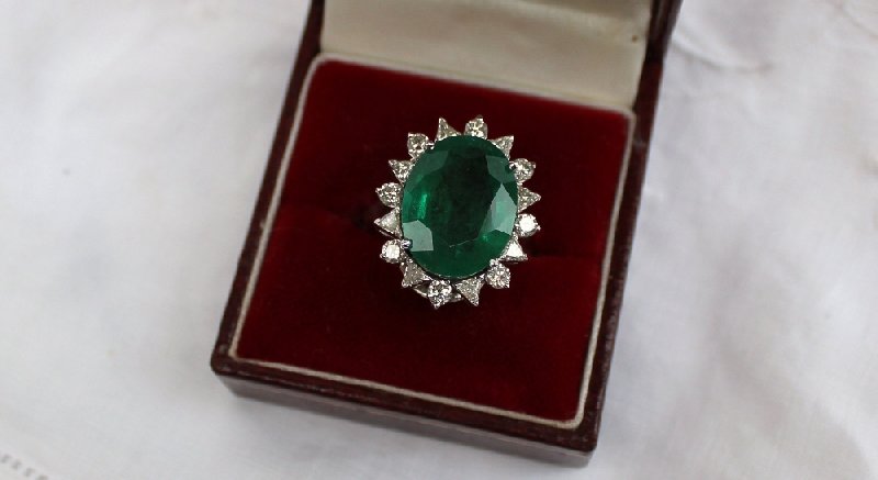 An emerald and diamond ring the central oval faceted emerald measuring 17mm x 13mm surrounded by