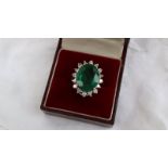 An emerald and diamond ring the central oval faceted emerald measuring 17mm x 13mm surrounded by