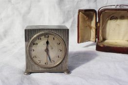 A Zenith white metal travel alarm clock, with line engraved decoration on flattened bun feet, the