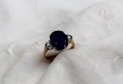 A sapphire and diamond ring the central oval faceted sapphire measuring 12mm x 9mm flanked by two